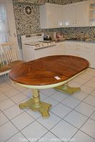 View of round wooden kitchen table with two painted pedestal supports in kitchen setting, showing table top surface and the overall structure.