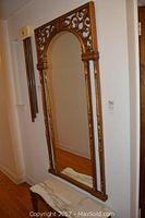 Full view of the large wall pier mirror showing gold leaf ornate frame and arched top, placed in hallway.