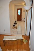 View of wooden bench with curved marble top and brass tone torchiere floor lamp standing next to it.