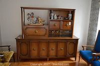 Full frontal view of the vintage fruitwood dry bar entertainment center with upper display shelves and lower cabinet doors visible, showing decorative brass hardware and carved details.