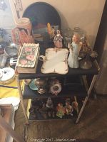 Front view of the three shelf rolling metal serving cart with various decorative items on top, middle, and bottom shelves including figurines, trays, and vases.