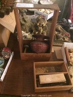 Photo showing the wooden shoe shine box with brushes and red applicator container inside, surrounded by decorative items in the background.