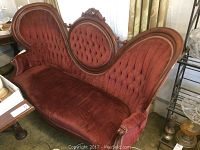 Full view of Victorian camel back sofa with red velvet upholstery and wood frame in a room, showing tufted cushions and carved wooden frame