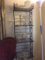 Glass serving ware displayed on black metal two-tiered serving rack with scroll designs, includes glass vase, cake plate, covered bowl, apothecary jar.