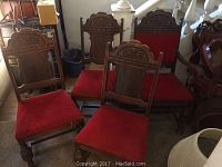 Four wood dining chairs grouped showing red velvet-like cushions and carved wooden backs, one with arms.