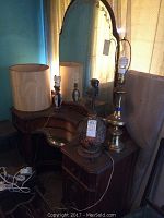 Front angle showing solid wood vanity dresser with attached mirror, lamps and small objects on top, placed near window with curtains.
