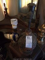 Two ceramic table lamps shown on a wooden table in front of a mirror, one taller with floral painted body and screw-type bulb installed; the smaller lamp is shorter and darker in color.