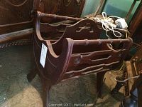 Front and side view of dark wooden magazine rack showing curved side handles and decorative side panels, scratches and finish wear visible.