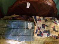 Photo showing a handmade quilt with rooster patchwork, a blue chenille bedspread, and part of a carved wooden headboard behind them.