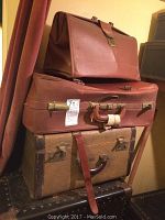 Stack of three brown luggage pieces, showing metal clasps, handles, and wear damage on the top piece