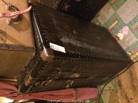 Closed view of the black vintage steamer trunk showing metal studs and scuffed top surface.