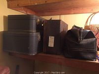 Four luggage pieces on a wooden shelf: two hard cases stacked on left, one medium textured case with label in center, black doctor's bag satchel on right