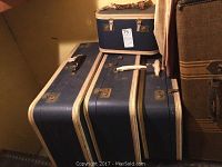 Four blue luggage pieces stacked, showing white trim, leather straps, and handles with wear and damage