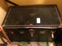 Closed black steamer trunk showing metal hardware, lock, and studded edges.