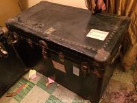 Large black vintage steamer trunk closed showing metal latches and reinforcements with visible wear