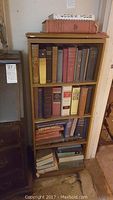 Full view of wooden bookcase filled with various vintage books across three shelves and top shelf with additional books.