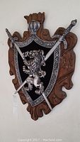 Full view of the coat of arms mounted on wall showing shield with lion and crossed sword and scepter mounted on wood-like backing