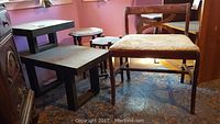 View of upholstered bench, two black wood tables of different sizes, and wooden side table on carpeted floor