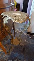 Full view of ornate metal plant stand or side table with curved legs and openwork top, gold-toned metal.