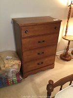 Full view of the solid wood four drawer chest of drawers against a wall with a lamp and other furniture nearby.
