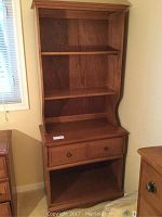 Front view of wood cabinet and bookshelf showing upper removable shelf, drawer with knobs, and lower open shelf.