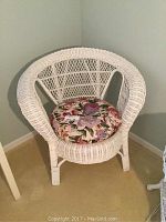 Front side view of white wicker chair with a floral round cushion, showing detailed weaving and chair shape.