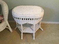 Front view of the white wicker side table showing oval top, decorative open loop band, and lower shelf with rounded legs.