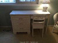 White wooden desk with drawers next to a white wooden chair, both placed in a room with carpet flooring.