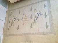 Reversible flatwoven area rug side one showing green bird motifs with stylized branches in blue and tan on a light beige background with fringe.