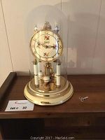 Full view of the Schatz anniversary clock with its glass dome cover in place, showing the floral dial, ornate design, and the winding key beside it.