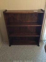 Front view of solid wood bookshelf showing three fixed shelves and dark wood finish.