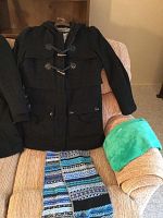 Front view of the black Guess women's winter coat hanging on a chair next to two scarves, one patterned knit and one solid teal.