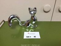 Front view of polished aluminum fox sculpture with curled tail and smooth, reflective surface.