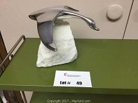 Front view of polished aluminum goose sculpture mounted on white stone base on green surface.