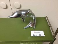 Front angled view of polished aluminum dolphin sculpture placed on green surface.