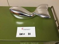 Polished aluminum whale sculpture on green surface, showing rounded body and tail fin, labeled lot number 51.