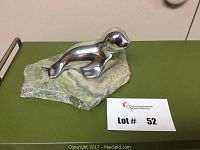Overall view of polished aluminum seal sculpture mounted on an irregular natural stone base with Lot card number 52 present.