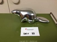 Polished aluminum beaver sculpture on green surface with lot number card nearby.