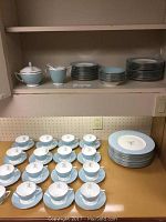 Wide view of multiple plates stacked and arranged with tea cups and saucers displayed beneath.