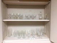 Shelf display showing a variety of crystal stemmed goblets, tumblers, and a decanter with stopper.