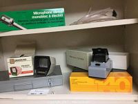 Shelf with metal slide storage case, Unarama slide viewer box, Precám viewer on orange Transvue 140 carousel slide tray box, and stereo microphone box on top shelf.