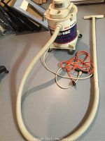 Full view of the beige and blue shop vac with attached hose, beige wand, and orange power cord arranged on the floor.