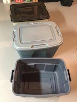 Three plastic storage totes shown on floor; one translucent with black lid, two opaque gray with one gray lid and one without lid