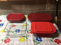 Four glass baking dishes displayed on a floral tablecloth. Three dishes have red plastic lids, one is without a lid.