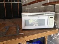 Whirlpool microwave hood range fan displayed on wooden surface with mounting bracket lying in front.