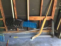 Two snow shovels with wooden handles, one black and one blue scoop, along with vintage wooden hockey goalie stick and roof snow shovel with metal handles.