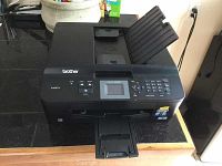 Front view of black Brother MFC-J425W 3-in-1 inkjet printer on black countertop showing input and output trays extended, control panel with LCD screen and numeric keypad visible.