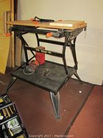Full view of the Black & Decker Workmate 400 work center, showing the folding legs, wood top clamped surface, and lower plastic shelf with some tools stored.