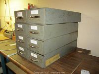 Photo of stack of 4 gray metal tool storage bins showing front and side, placed on table in basement workshop.