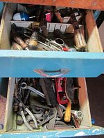 Top drawer containing wooden handled screwdrivers, scissors, pliers, file, measuring tape, and various small hand tools with some paint wear and grime.